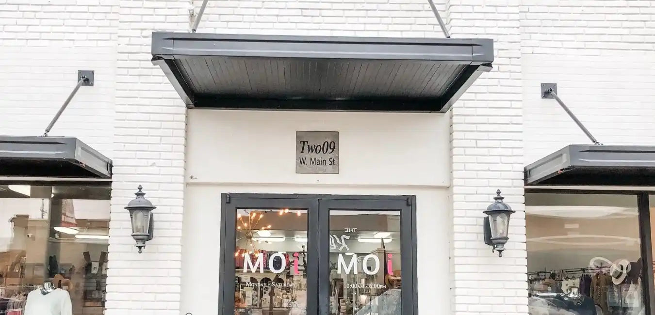 The entrance of a boutique with a dark awning and double glass doors.
